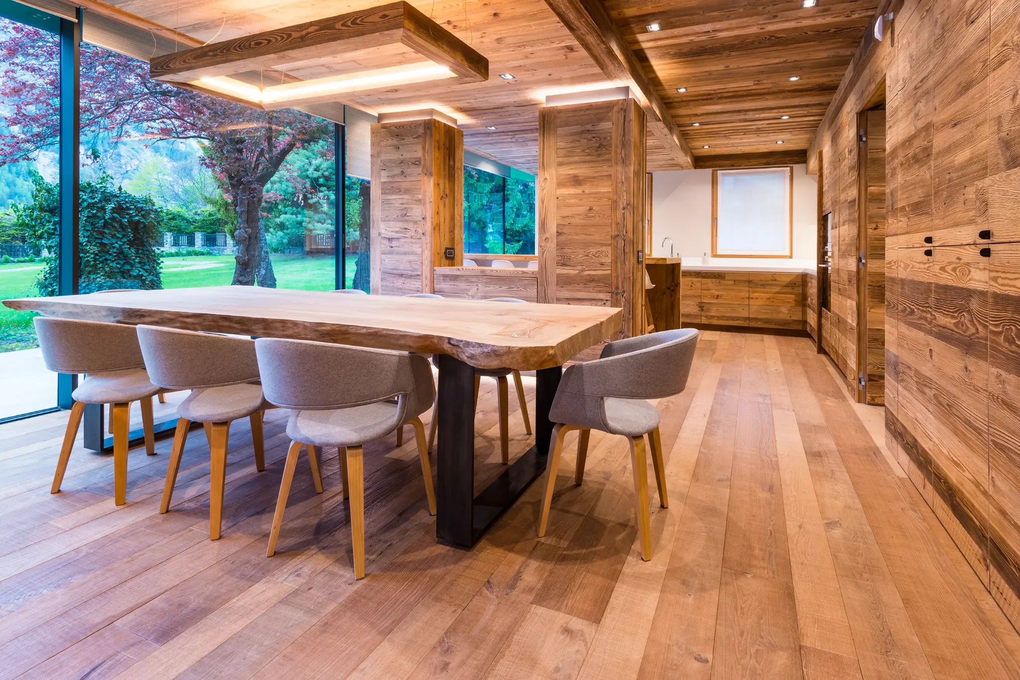 Open space con grande tavolo in legno, cucina e vetrate sul giardino